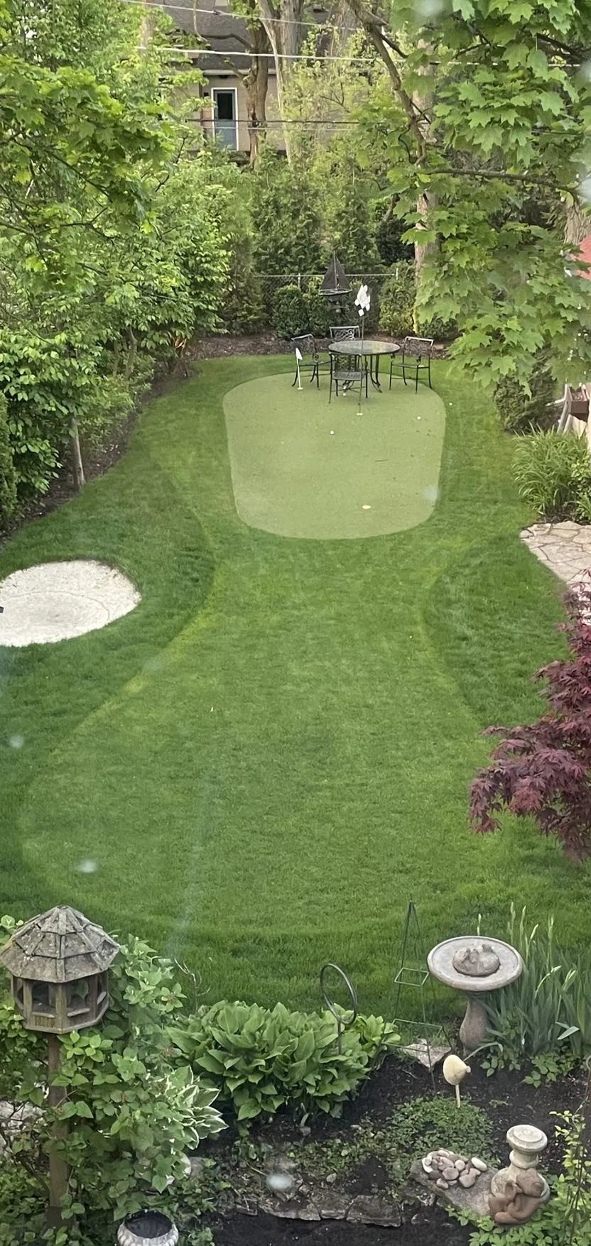 Backyard with an artificial putting green, patio table, and garden beds