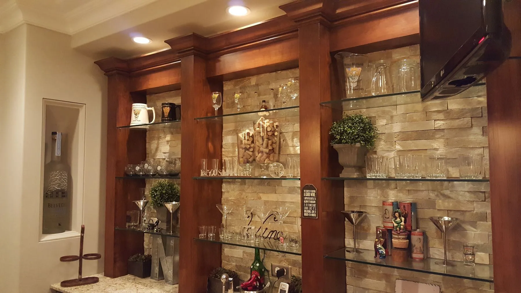 Bar with glass shelves, a stone wall, and wood columns