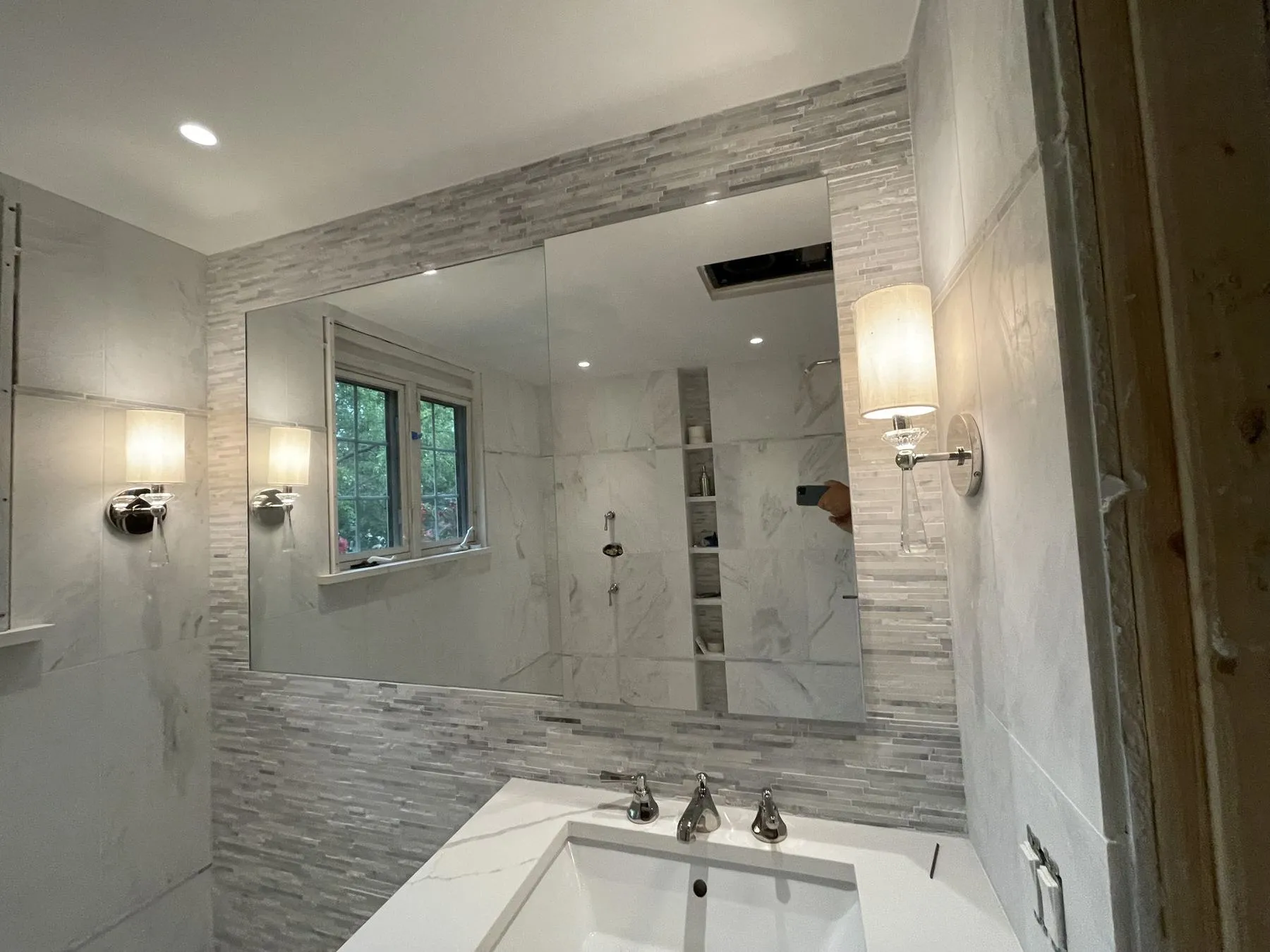 Bathroom vanity under a wide mirror framed in stone tile