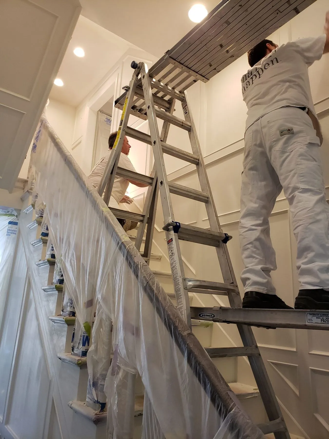 Painters finishing paneled walls along a staircase, with the stairs protected