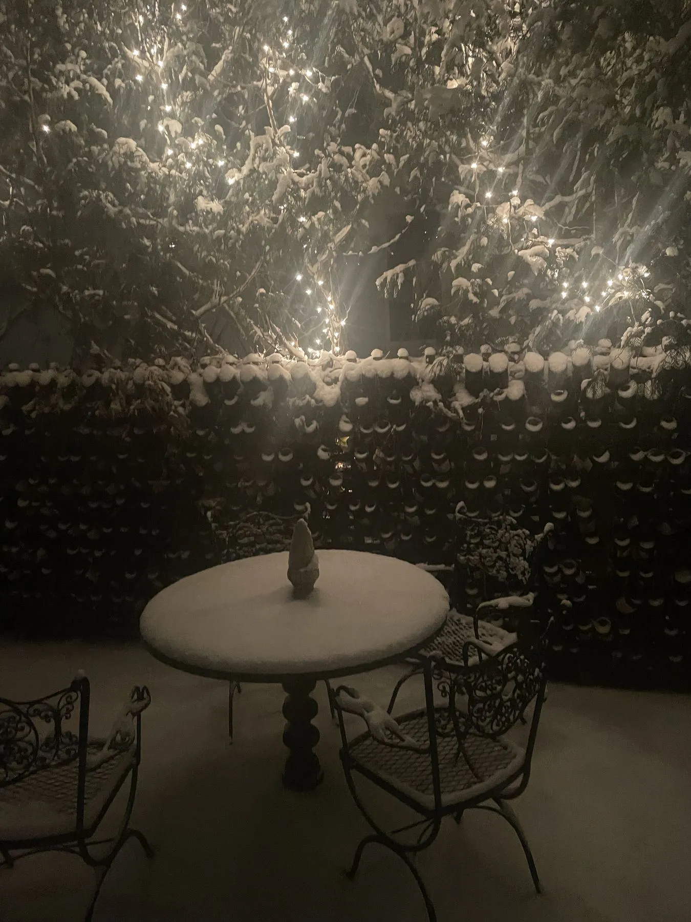 Fence built from wine bottles, lit at night behind a patio table